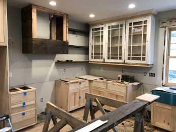 The custom reclaimed hood and shelves are being installed next to the reclaimed glass door cabinets.